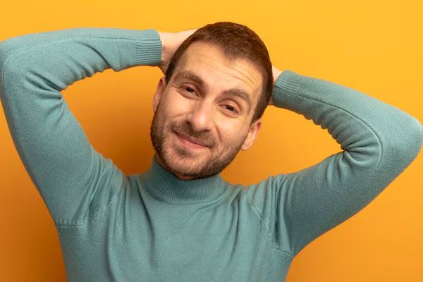 giovane uomo sorridente che guarda avanti mettendo le mani dietro la testa - miglior trapianto capelli Italia