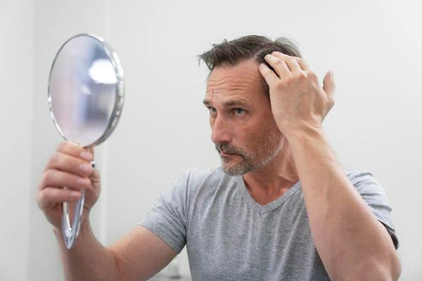 uomo che si guarda allo specchio mentre si tocca i capelli con una mano.