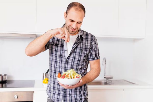 Uomo sorridente che condisci con sale un'insalata in cucina - Alimentazione e trapianto di capelli
