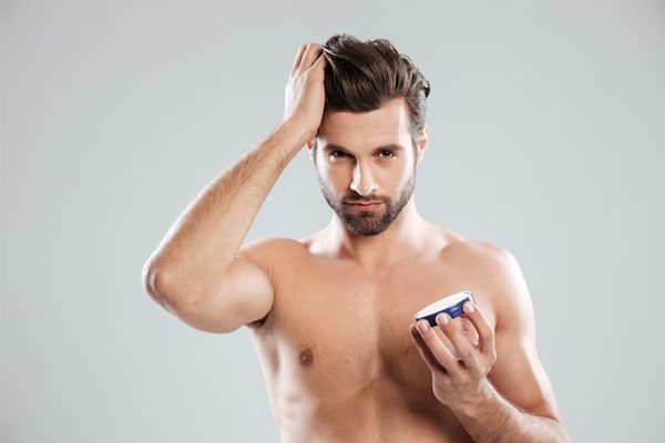 bell'uomo con una mano tra i capelli e l'altra che tiene un contenitore di crema - - trapianto capelli Italia