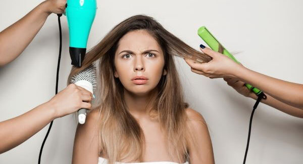 Una donna preoccupata si asciuga i capelli con un asciugacapelli, una piastra e una spazzola.
