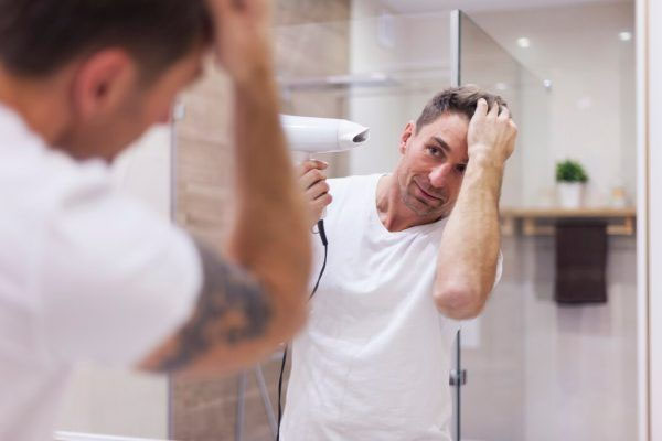 Uomo che usa un asciugacapelli davanti allo specchio